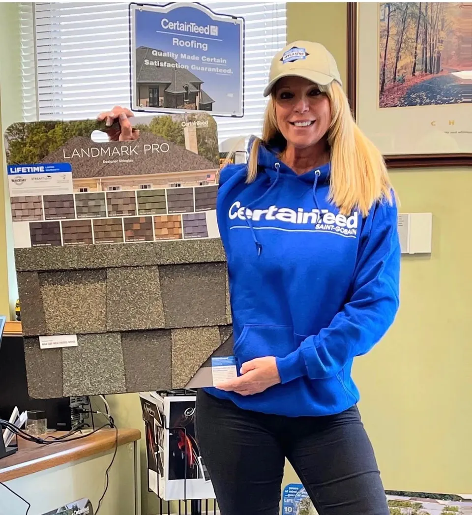 Toni Bryan wearing a CertainTeed sweatshirt and SELECT ShingleMaster cap beside a Landmark Pro shingle display board